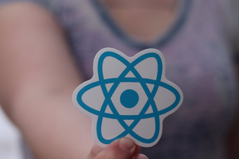 Close-up of a silver MacBook laptop displaying a dark-themed code editor on a white desk. To the left of the laptop, there is a white notebook with a silver pen resting on it, and a white smartphone i